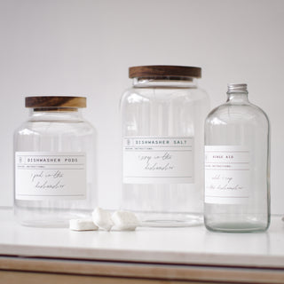 Three clear glass jars with wooden lids, labeled respectively for Dishwasher Pods, Dishwasher Salt, and Rinse Aid.