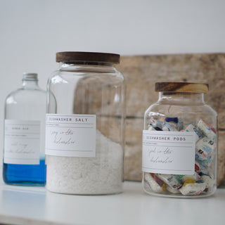 Three clear glass jars with wooden lids, labeled respectively for Dishwasher Pods, Dishwasher Salt, and Rinse Aid.
