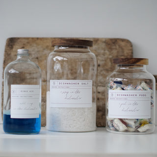 Three clear glass jars with wooden lids, labeled respectively for Dishwasher Pods, Dishwasher Salt, and Rinse Aid.