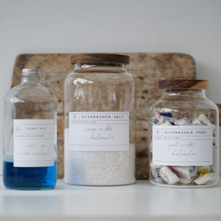 Three clear glass jars with wooden lids, labeled respectively for Dishwasher Pods, Dishwasher Salt, and Rinse Aid.