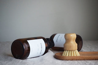Two amber glass soap bottles with black pump lids labeled 'HAND SOAP' and 'DISH SOAP' on a wooden tray, alongside a wooden dish brush.