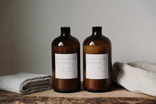 Amber bottles of fabric softener and fabric softener on a wooden surface with a neutral background