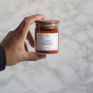 Hand holding a jar of chili powder against a neutral background
