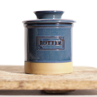 Blue ceramic butter container with gold base on a wooden surface
