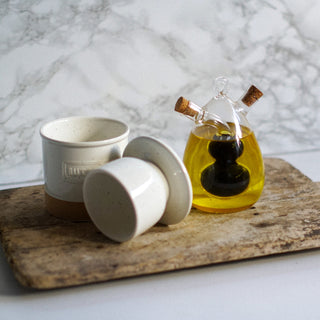 White ceramic containers and a glass bottle with cork lid on a wooden board against a marble background