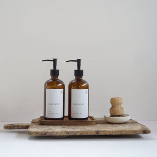 Two brown bottles with labels on a wooden tray against a white background