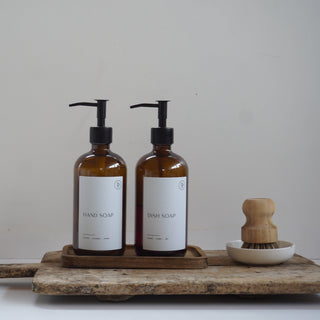 Two brown bottles with pump dispensers on a wooden tray against a white background