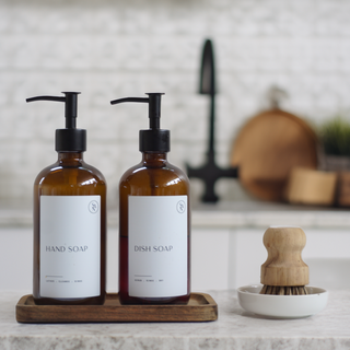 Two brown soap dispensers labeled 'Hand Soap' and 'Dish Soap' on a wooden tray with a kitchen background.