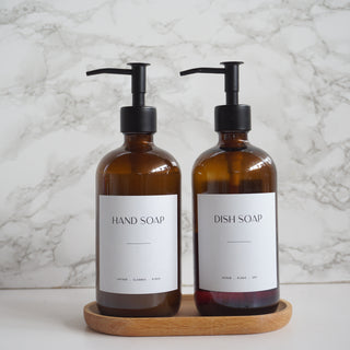 Two brown soap bottles with pump dispensers on a wooden tray against a marble background.