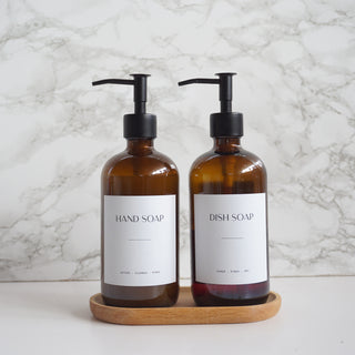 Two brown soap bottles with pump dispensers on a wooden tray against a marble background.