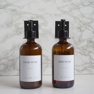 Two amber glass soap dispensers labeled 'Hand Soap' and 'Dish Soap' on a marble background.