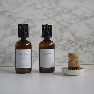 Two bottles of hand soap and dish soap with a brush holder on a marble background