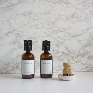 Two bottles of hand soap and dish soap with a brush on a marble countertop