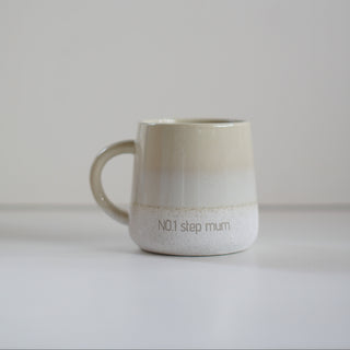 A ceramic mug with a beige-to-white gradient glaze, featuring the text 'NO.1 step mum' printed on the front, set against a minimalist light gray background.
