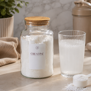 Glass jar of creatine with a glass of water on a marble surface