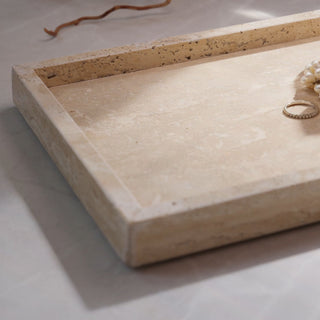 Beige travertine stone jewellery tray with a ring on a light background