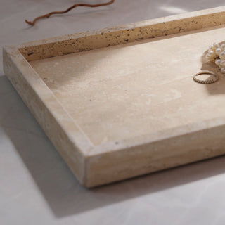 Beige stone jewelry tray with a ring and pearl necklace on a light background
