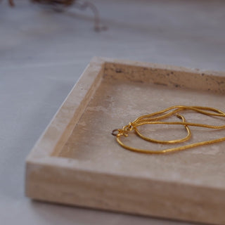 Jewellery including a gold necklace, pearl earrings, and a Chanel perfume bottle on a travertine marble tray.